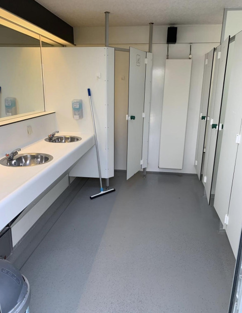 Toilettes publiques propres avec lavabos, miroir, outil de nettoyage et cabines fermées dans un parc néerlandais.