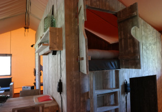Interior de una tienda safari con cama elevada de madera, iluminación cálida y muebles rústicos.