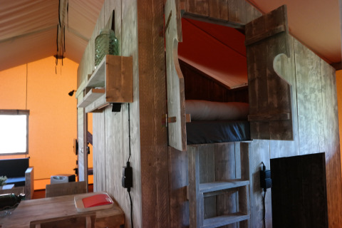 Interior of a safari tent featuring a rustic wooden loft bed, cozy lighting, and wooden furniture.