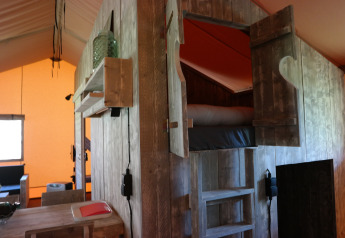 Interno di una tenda safari con letto in legno rialzato, atmosfera accogliente e arredi rustici.
