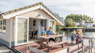Familie hygger sig udenfor en chalet ved Marina Parcs Almere, med udsigt over vandet i Holland.