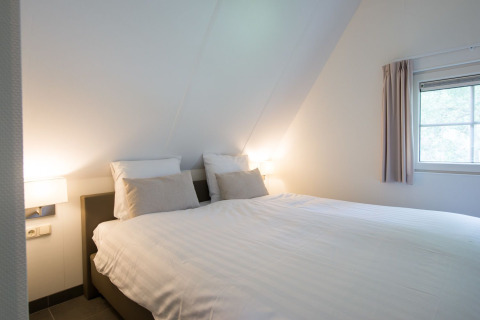 Dormitorio con cama doble, sábanas blancas y luz suave en Wellness Lodge XL, Hof van Salland, Países Bajos.