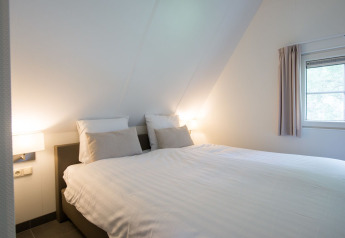 Chambre avec lit double, draps blancs et lumière douce au Wellness Lodge XL, Hof van Salland, Pays-Bas.