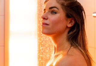 Mujer disfruta de una ducha relajante con luz cálida en Wellness Lodge en Hof van Salland, Países Bajos.