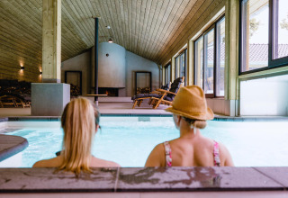 Dos mujeres se relajan en la piscina cubierta de Wellness Lodge XL, Hof van Salland, Países Bajos, con vista al jardín.