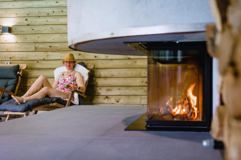 Donna che si rilassa vicino al camino nella Wellness Lodge XL, Hof van Salland, Paesi Bassi.