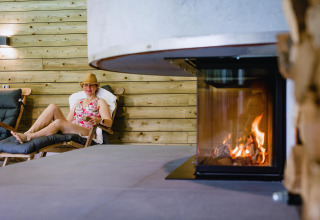 Mujer relajándose en silla junto a chimenea en Wellness Lodge XL, Hof van Salland, Países Bajos.