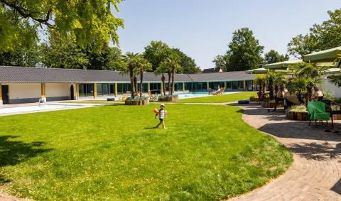 Ampio prato verde con piscina centrale, circondato da tiny house e palme in una giornata soleggiata.