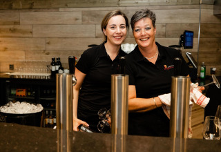 Dos mujeres sonrientes con camisas negras trabajan detrás de la barra de un restaurante tiny house.
