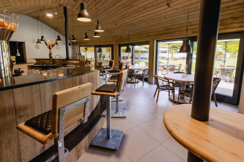 Interior de cafetería moderna en tiny house, con taburetes, techo de madera y ventanales al jardín.