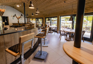 Interior de cafetería moderna en tiny house, con taburetes, techo de madera y ventanales al jardín.