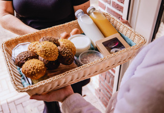 Cesta de desayuno con panecillos, leche, jugo, huevos y yogur entregada en la puerta de una tiny house.