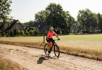 Persoon fietst op een zandweg voor kleine huisjes met grasveld op een zonnige dag in het dorp.