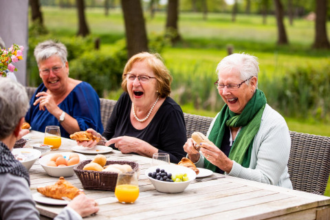 Mujeres mayores ríen y disfrutan del desayuno al aire libre en Wellness Lodge XL en Hof van Salland, Países Bajos.