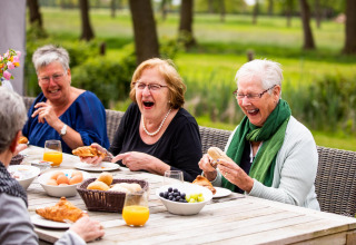 Mujeres mayores ríen y disfrutan del desayuno al aire libre en Wellness Lodge XL en Hof van Salland, Países Bajos.