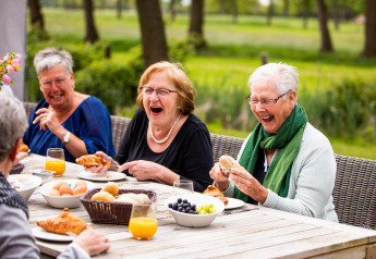 Mujeres mayores ríen y disfrutan del desayuno al aire libre en Wellness Lodge XL en Hof van Salland, Países Bajos.