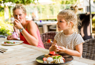 Una niña pequeña come postre junto a una mujer en una mesa exterior en Wellness Lodge XL, Hof van Salland.