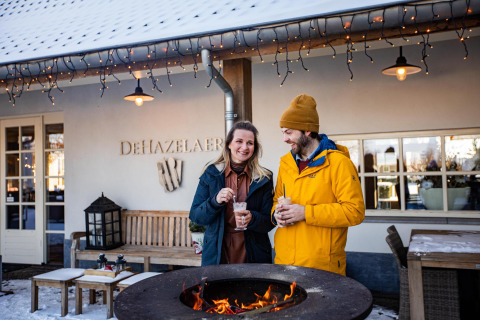 Una coppia gusta bevande calde accanto al fuoco fuori dalla Wellness Lodge XL, Hof van Salland, Paesi Bassi in inverno.