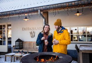 Una pareja disfruta bebidas calientes junto al fuego en Wellness Lodge XL, Hof van Salland, Países Bajos, en invierno.