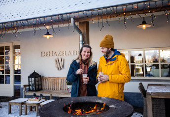 Un couple savoure une boisson chaude près d'un feu devant Wellness Lodge XL, Hof van Salland, Pays-Bas en hiver.