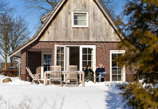 Pareja sentada fuera de Wellness Lodge XL en Hof van Salland, Países Bajos, rodeados de nieve.