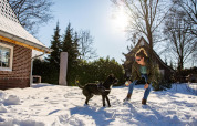 Vrouw speelt met een zwarte hond in de sneeuw bij Wellness Lodge XL in Hof van Salland, Nederland, op een zonnige dag.
