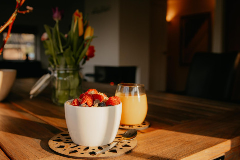 Un bol de yogur con bayas y un vaso de jugo sobre una mesa de madera en la cocina de una tiny house acogedora.