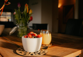 Un bol de yaourt aux fruits rouges et un verre de jus sur une table en bois dans une cuisine de tiny house.