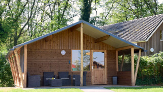 Houten kabine op Camping de Koeksebelt in Nederland met terras en veel omringend groen.