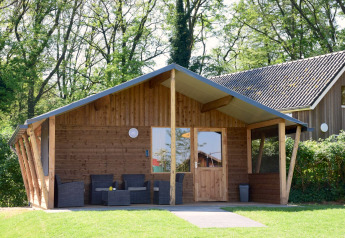Houten lodge bij Camping de Koeksebelt, Nederland, met overdekt terras en omgeven door bomen.