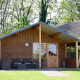 Holzhütte im Camping de Koeksebelt in den Niederlanden, mit Veranda und Garten umgeben von Bäumen.