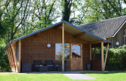 Cabaña de madera en Camping de Koeksebelt, Países Bajos, rodeada de vegetación y con terraza frontal.