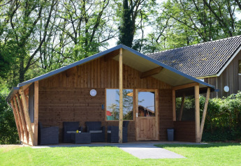 Wooden cabin at Camping de Koeksebelt in the Netherlands, with patio seating and surrounded by trees.