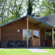 Wooden cabin at Camping de Koeksebelt in the Netherlands, with patio seating and surrounded by trees.