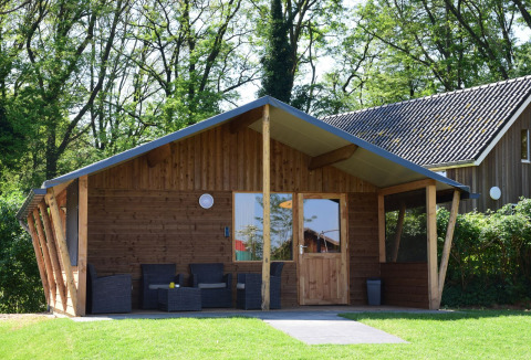 Holzhütte im Camping de Koeksebelt in den Niederlanden, mit Veranda und Garten umgeben von Bäumen.