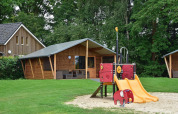Playground with slide in front of wooden cabins at Cabin, Camping de Koeksebelt in the Netherlands, forest view.