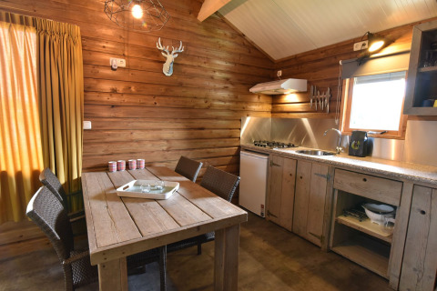 Interior de cabaña acogedora con paredes de madera, mesa de comedor, cocina y ventana en Camping de Koeksebelt, Países Bajos.