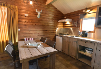 Træhytteinteriør med spisebord, køkken, vindue og rustikke møbler i Cabin på Camping de Koeksebelt, Holland.