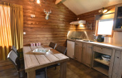 Knus interieur van een houten cabin met eettafel, keuken en raam bij Camping de Koeksebelt in Nederland.