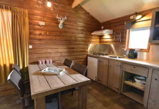 Interior de cabaña acogedora con paredes de madera, mesa de comedor, cocina y ventana en Camping de Koeksebelt, Países Bajos.