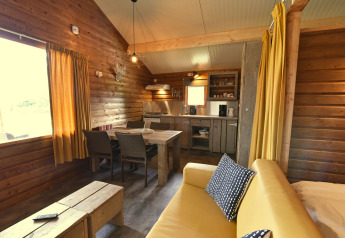 Cozy wooden cabin interior with dining area, kitchen, and sofa at Camping de Koeksebelt, Netherlands.