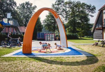 Kinderen spelen onder een grote oranje boog bij de speeltuin van de Cabin op Camping de Koeksebelt, Nederland.