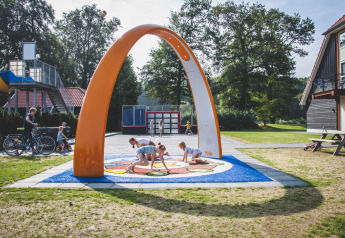 Children play under a large orange arch at the playground by the Cabin at Camping de Koeksebelt in the Netherlands.