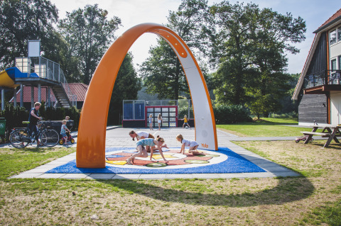 Kinder spielen unter einem großen orangen Bogen am Spielplatz der Cabin im Camping de Koeksebelt, Niederlande.