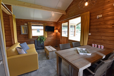 Vue intérieure d’une cabane chaleureuse au Camping de Koeksebelt avec canapé jaune et grande table en bois.