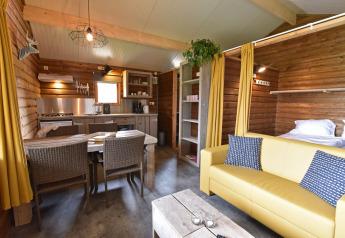Interior view of a cozy wooden cabin with kitchen, dining table, and sofa at Camping de Koeksebelt.