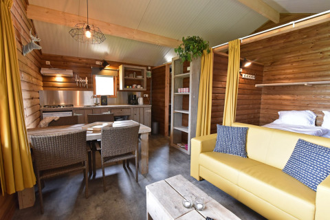 Vista interior de una acogedora cabaña de madera con cocina, mesa de comedor y sofá en Koeksebelt.