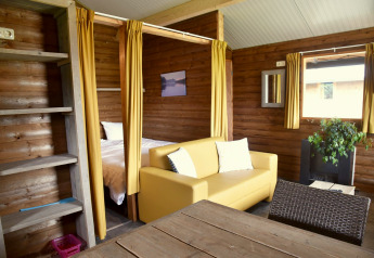 Gezellig hutinterieur op Camping de Koeksebelt in Nederland, met een gele bank en houten muren.