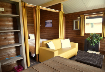 Knus interieur van een hut bij Camping de Koeksebelt in Nederland, met gele sofa en houten wanden.