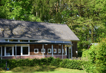Eine Hütte im Camping de Koeksebelt, Niederlande, mit Holzverkleidung, Fenstern und viel grünem Wald.